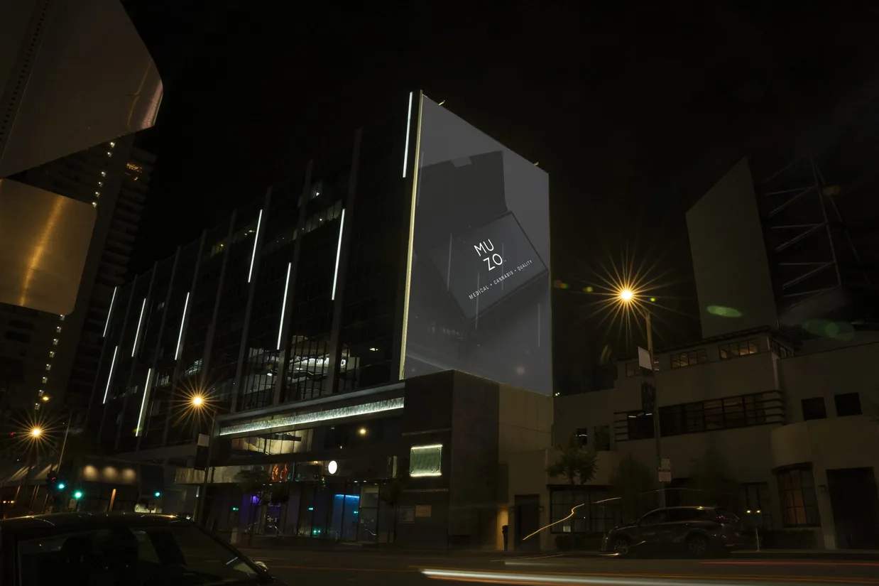 A city building at night, its glass face lit in strips, with a large MUZO board carrying the line Medical, Cannabis, Quality angled across its corner above the street