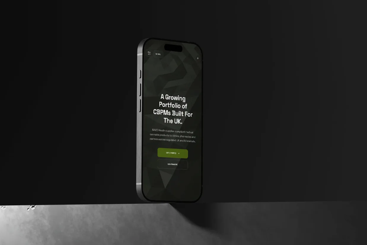 The MUZO Health home page on a phone standing on a grey ledge: A Growing Portfolio of CBPMs Built For The UK over the dark leaf ground