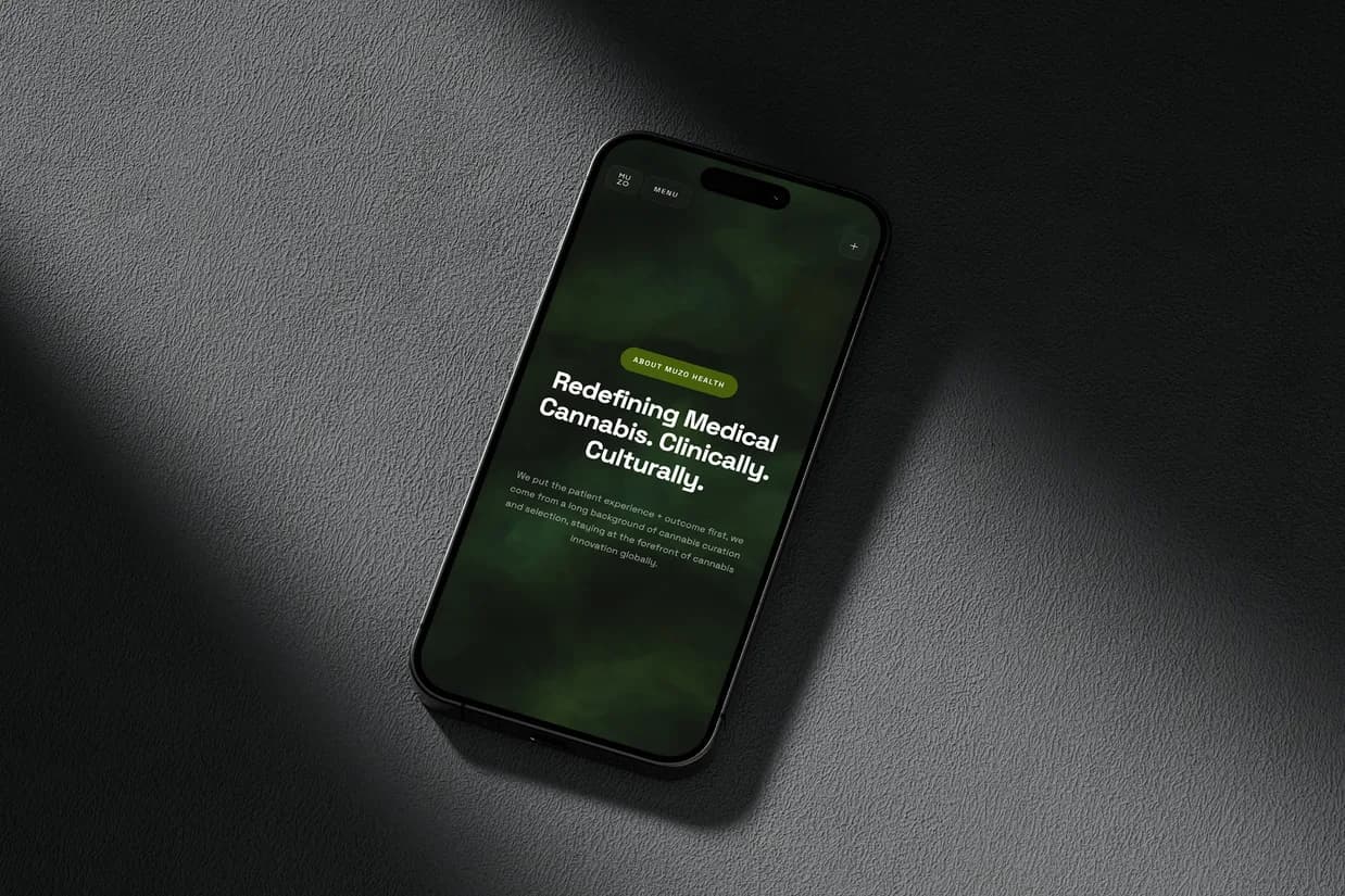 The MUZO Health About page on a phone lying on grey: the green panel reading Redefining Medical Cannabis. Clinically. Culturally.