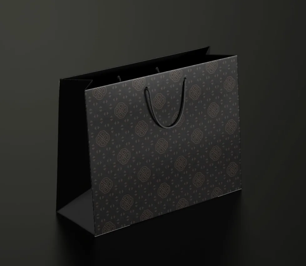 A black gift bag in the brand pattern with a rope handle