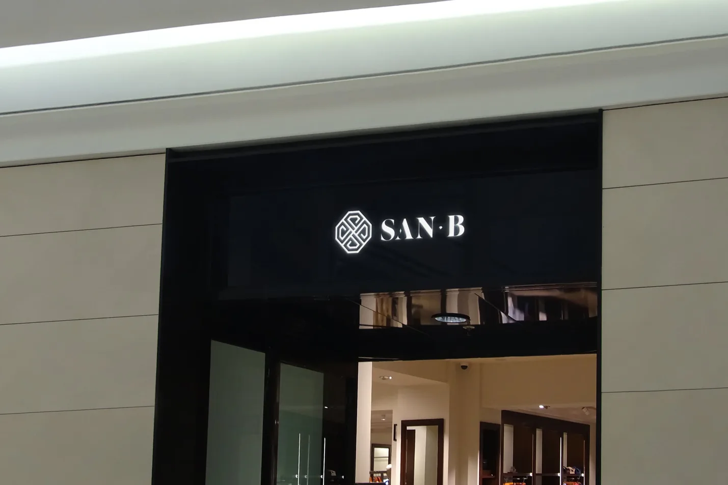 The emblem and SAN B lit on a black fascia over a shop entrance, stone walls either side