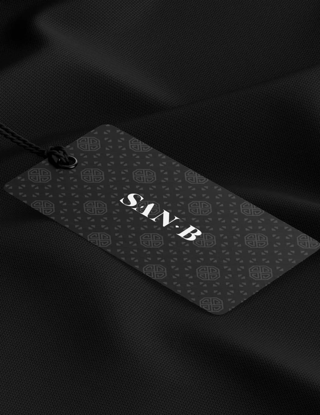 A patterned swing tag on black cloth, SAN B across it, its cord running up out of the frame