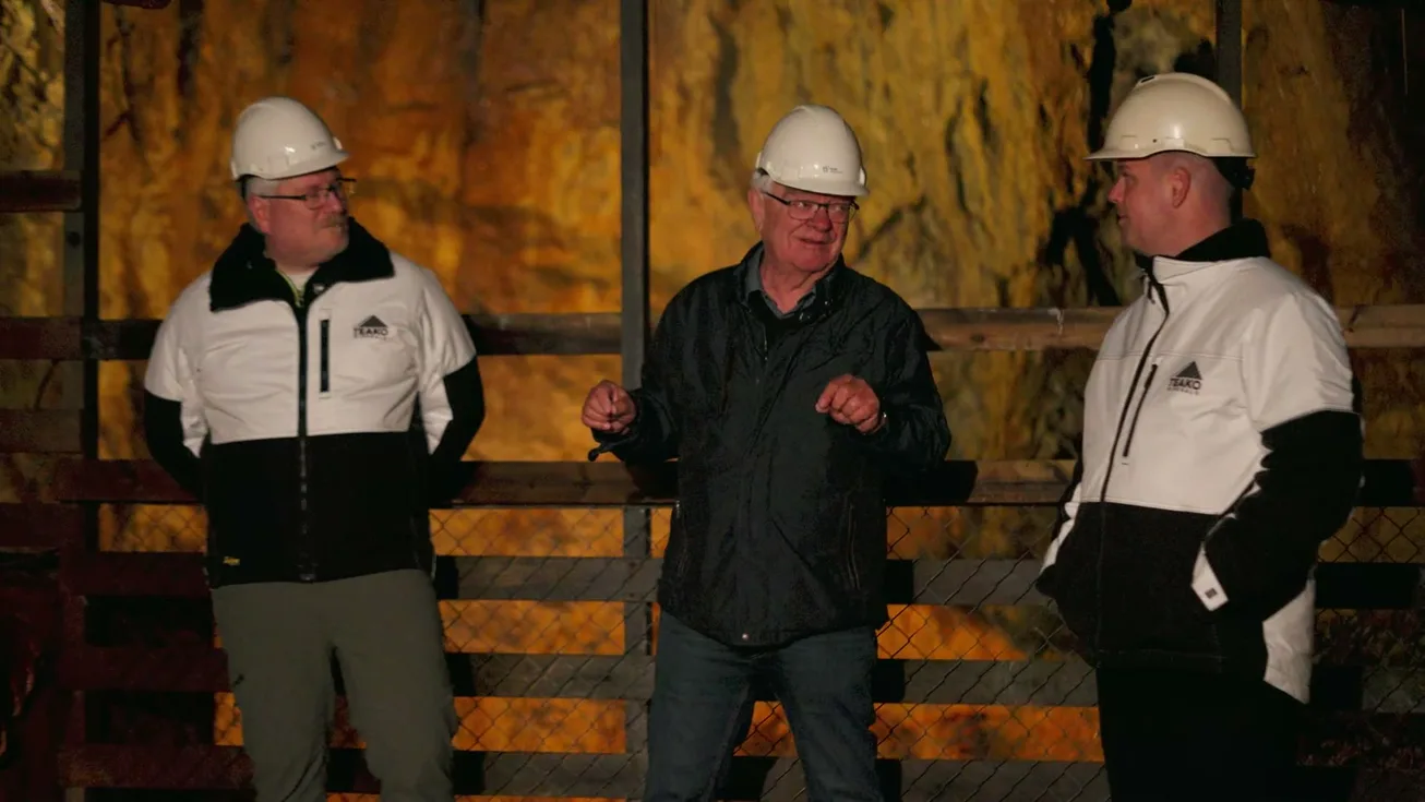 Three of the team in hard hats underground, the rock lit red behind them