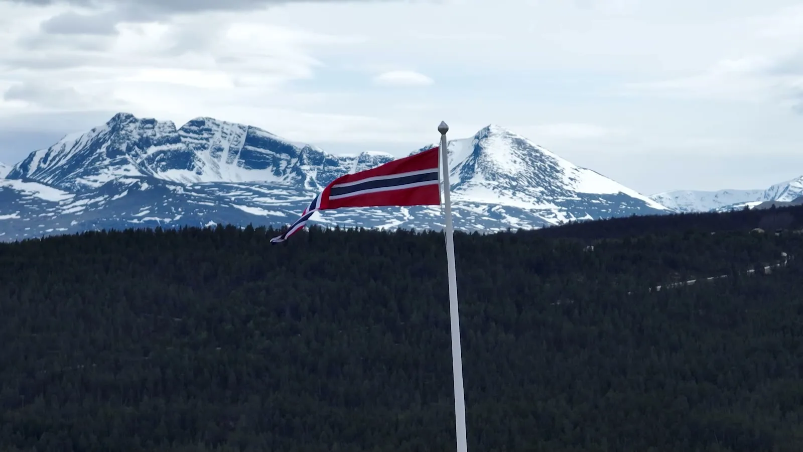 The Norwegian flag over the treeline, the snow range behind