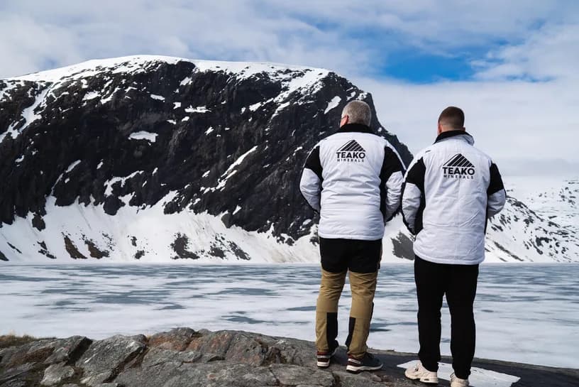 Two in Teako jackets on the shore of the frozen lake, the snow range across it