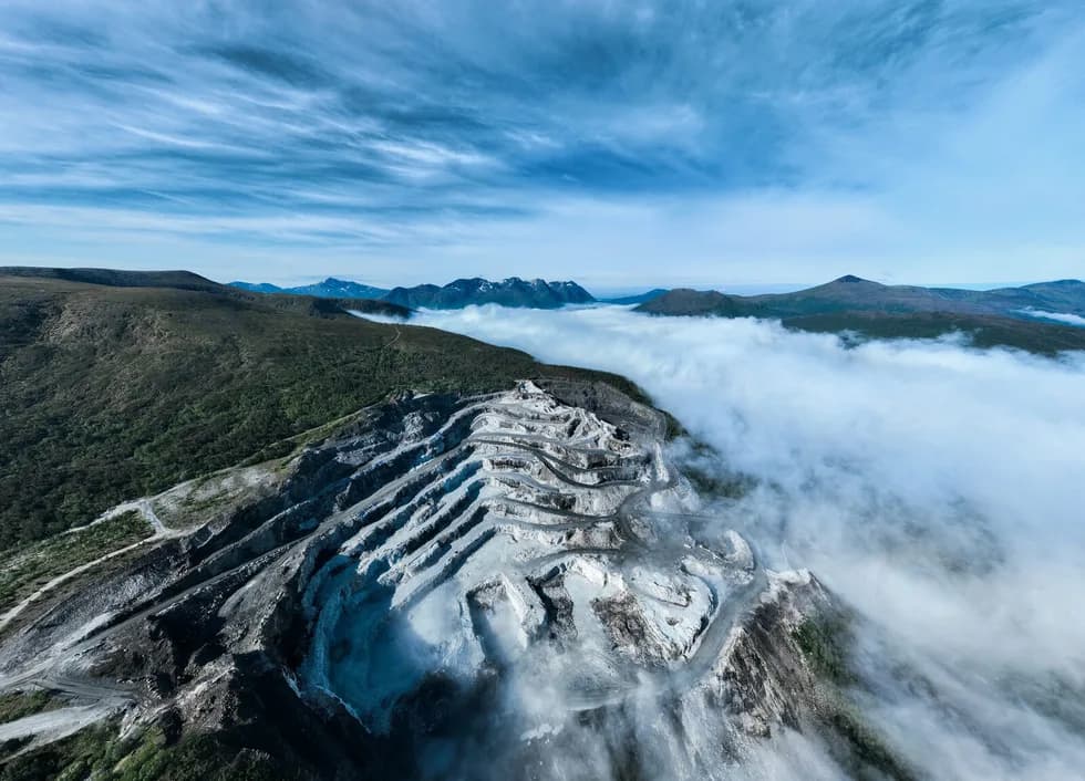 A quarry cut into the top of a ridge, cloud lying along the valley below it.