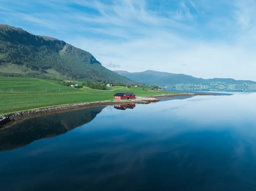 A farm on the fjord shore, the hill reflected in still water