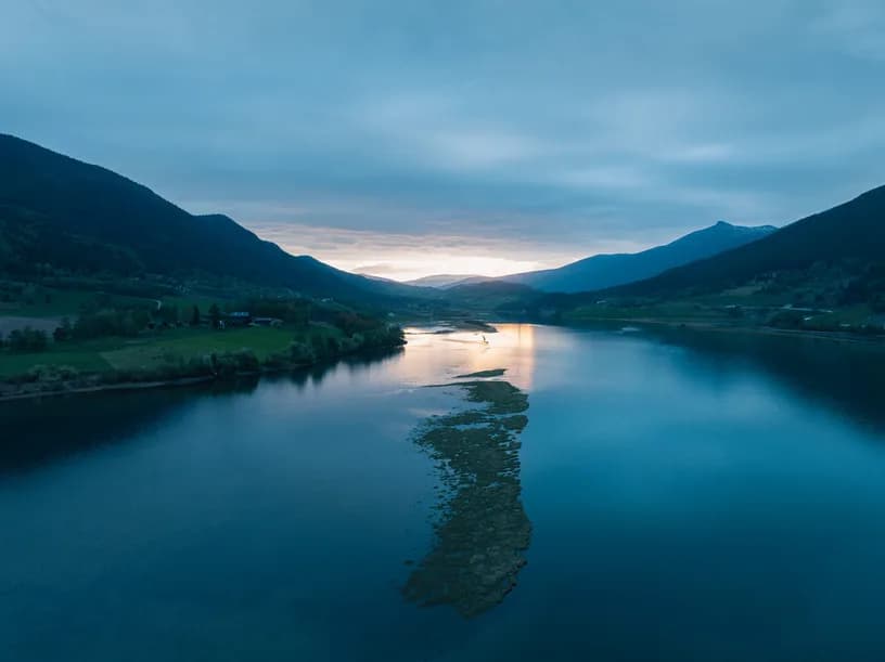 The lake at dusk, a spit of land reaching into still water and the last light behind the ridge