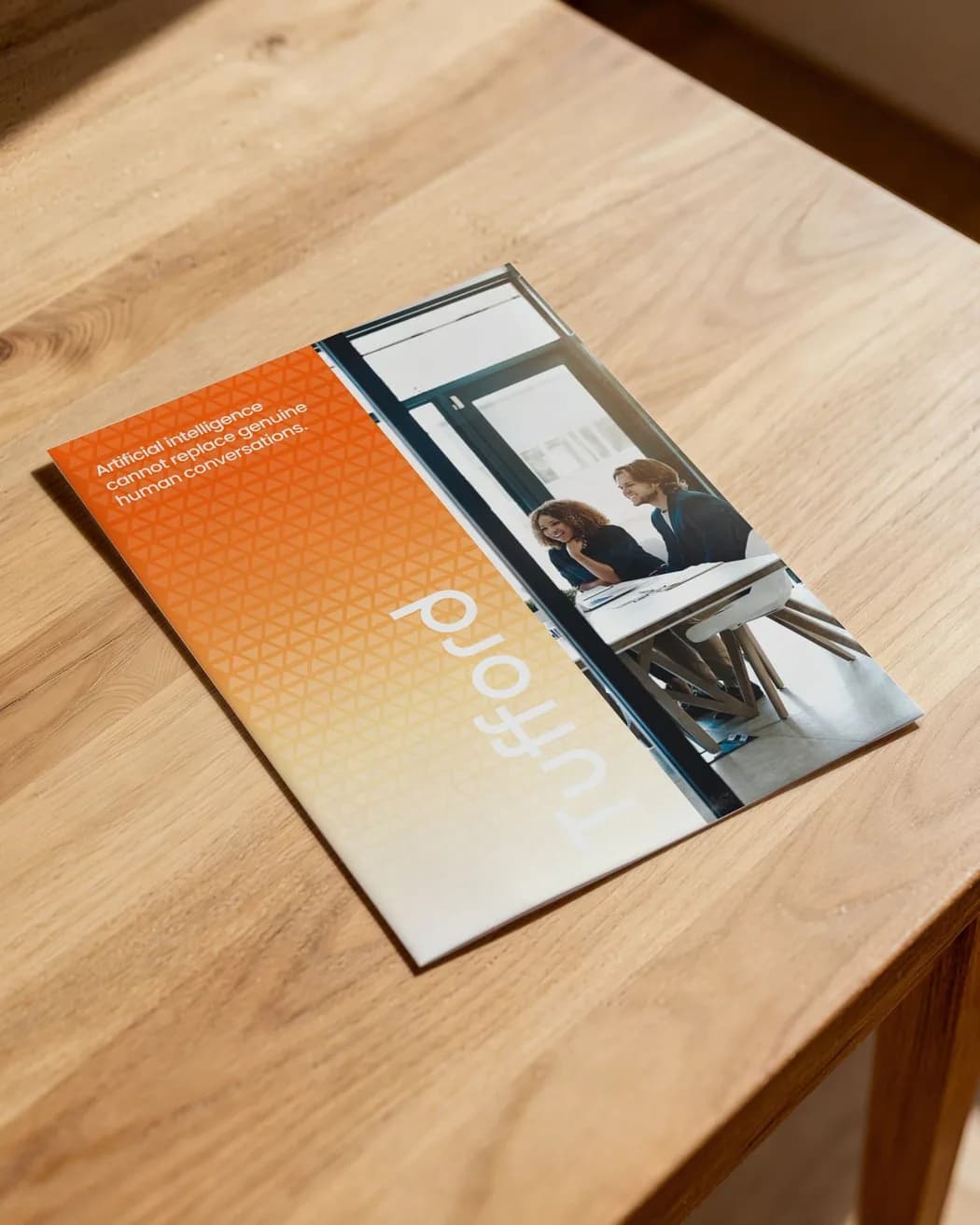The folded brochure on a wooden table: the pattern down its spine, the wordmark, two colleagues at a table, and the line about artificial intelligence