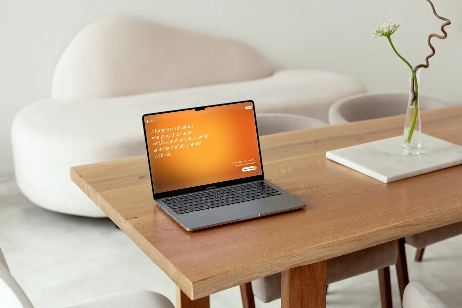 The Tufford home page on a laptop on a light oak table, a pale sofa behind it and a flower in a glass beside it: the opening line on the orange gradient