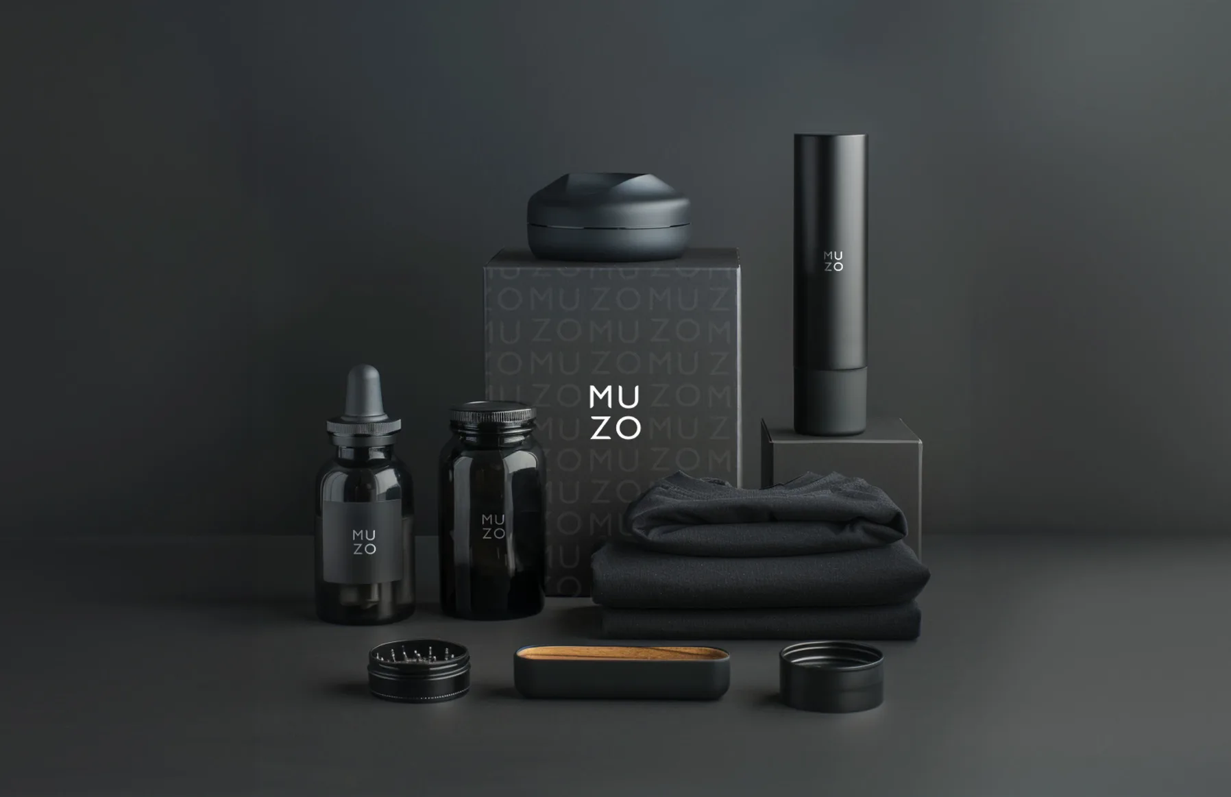 The MUZO range on a grey ground: the monogrammed box, two dropper bottles, the jar, a grinder, a wooden tray, a vaporiser and a folded black cloth