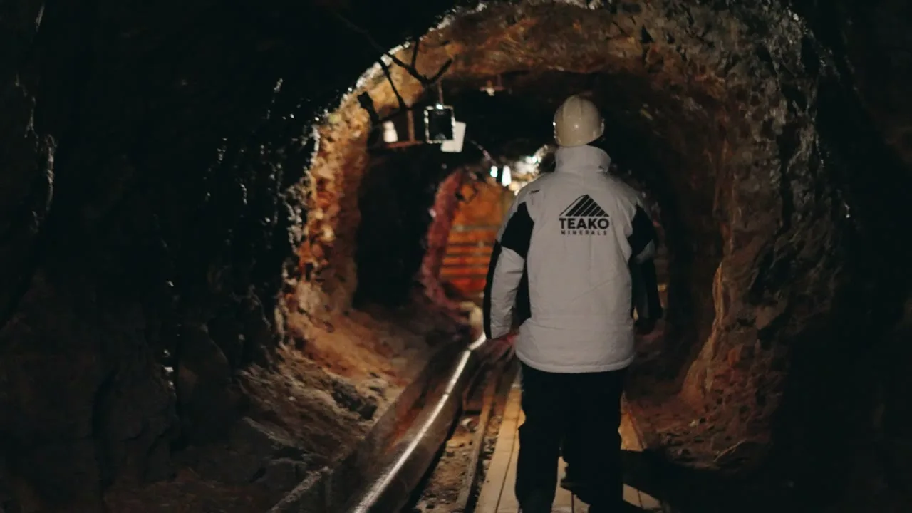 A geologist in a Teako Minerals jacket walking into the adit, the lit drift ahead of him: The Sleeping Giant, on location in Norway